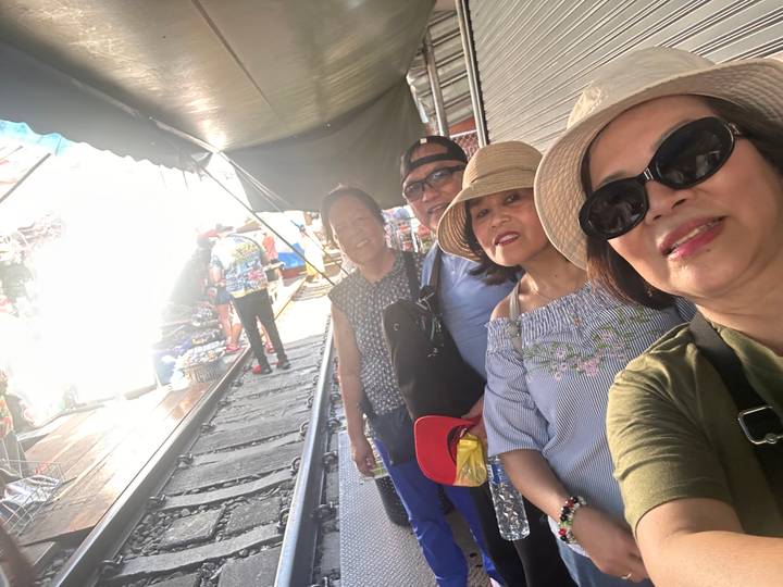 Selfie of travellers smiling beside stalls set up along the rail tracks at a market.