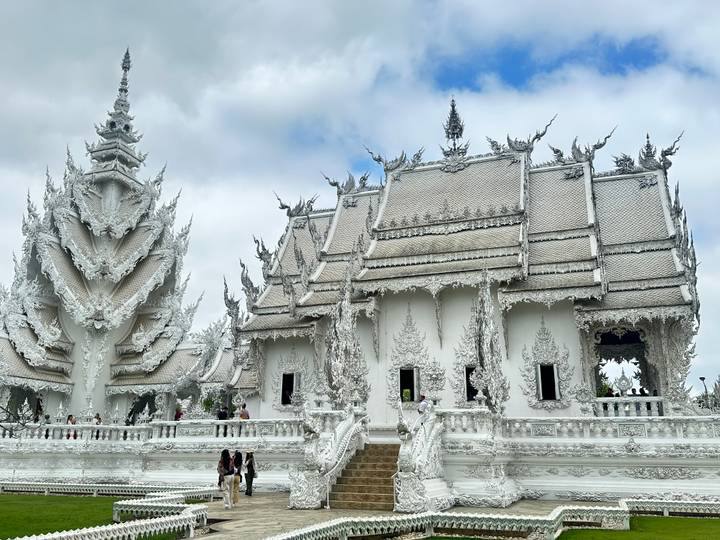 Intricately carved White Temple complex shimmering under bright light with visitors exploring.