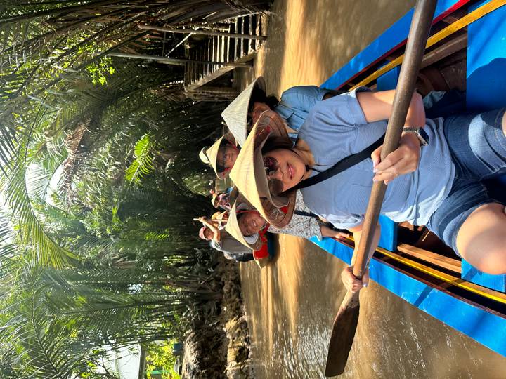Tourists paddling a narrow wooden boat through dense palm forest canals of the Mekong Delta.