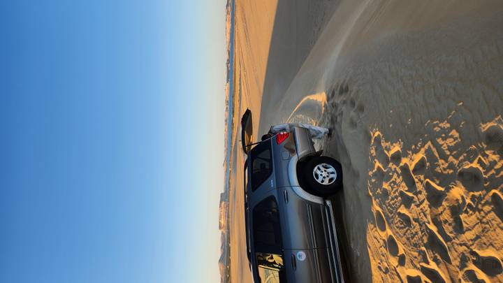 4x4 vehicle parked on rippling golden desert dunes at dawn with distant cliffs on the horizon.