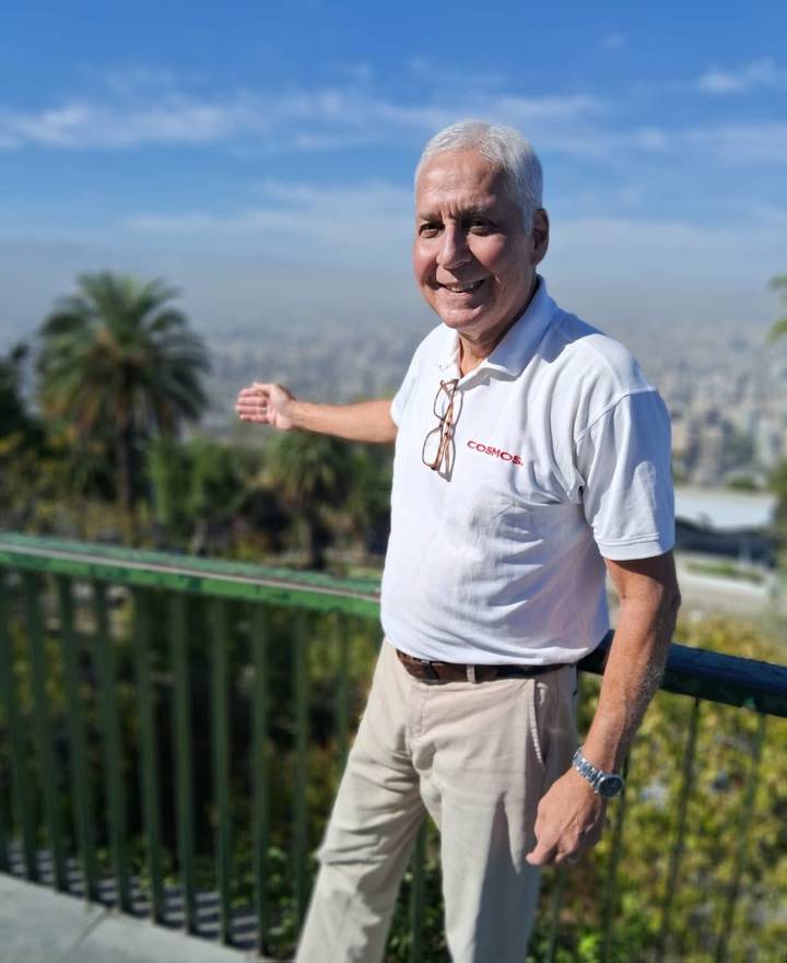Smiling tour guide gesturing towards a hazy city panorama while standing at a lookout railing