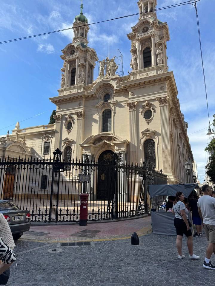 Historic sandstone church facade bordered by wrought-iron fencing on a sunny urban street