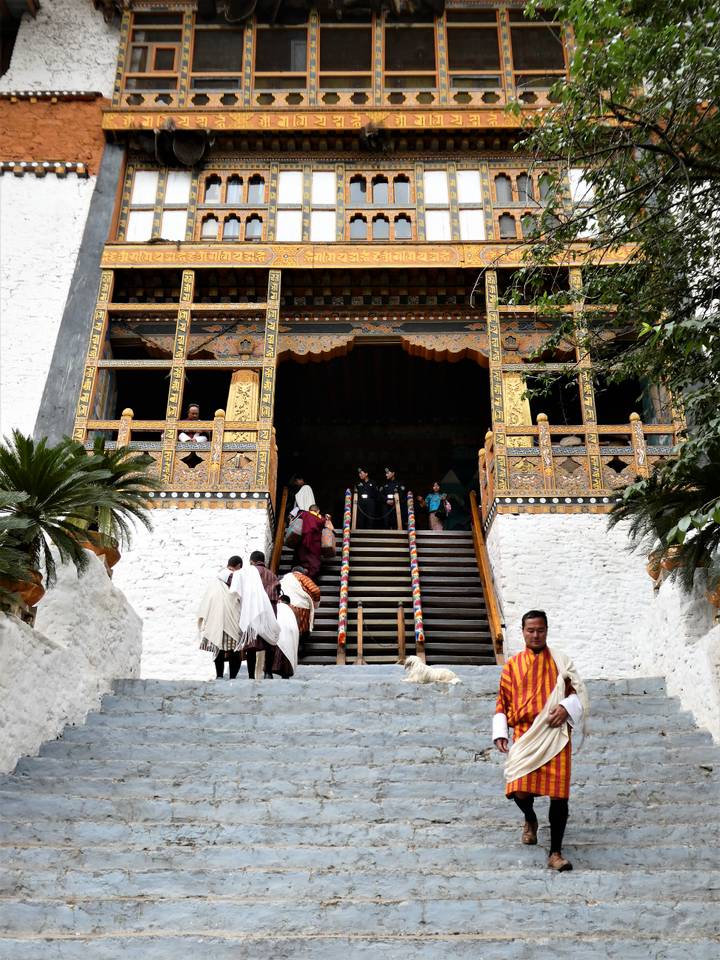 Visitors ascending the ornate staircase of a Bhutanese dzong with carved wooden balconies.