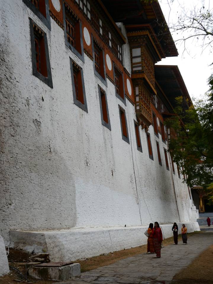 Long whitewashed exterior wall of a Bhutanese dzong lined with small wooden windows.