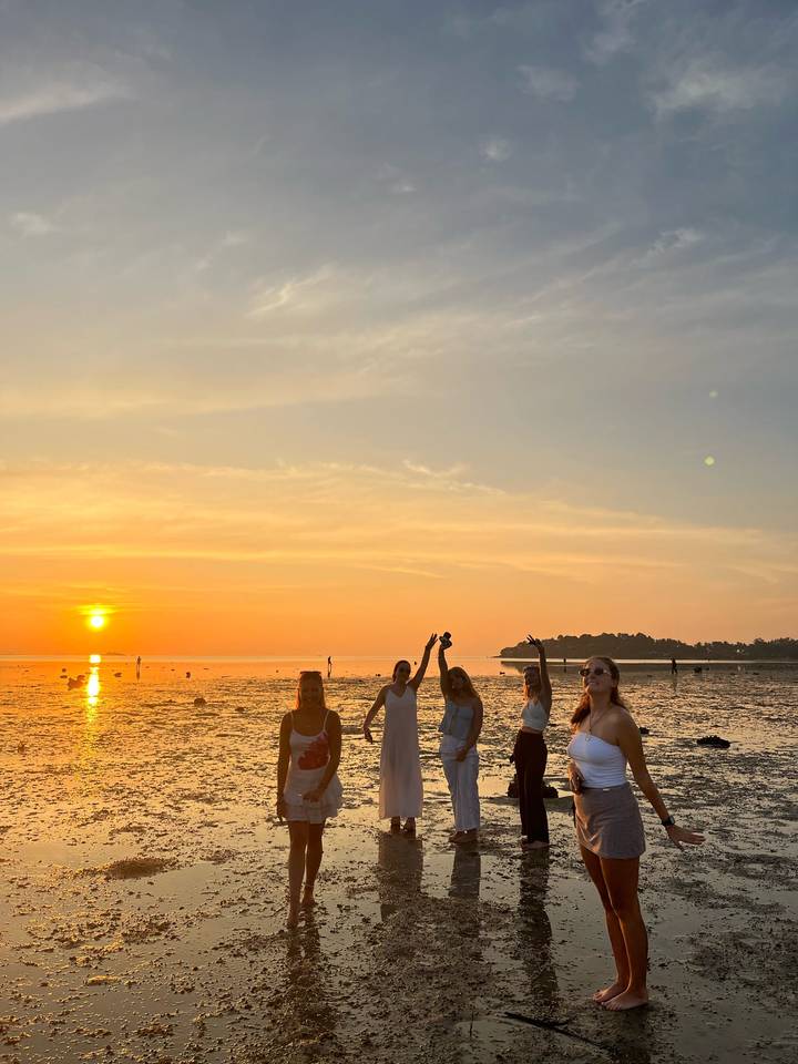 Group of friends celebrating on a tidal flat during a vivid beach sunset.