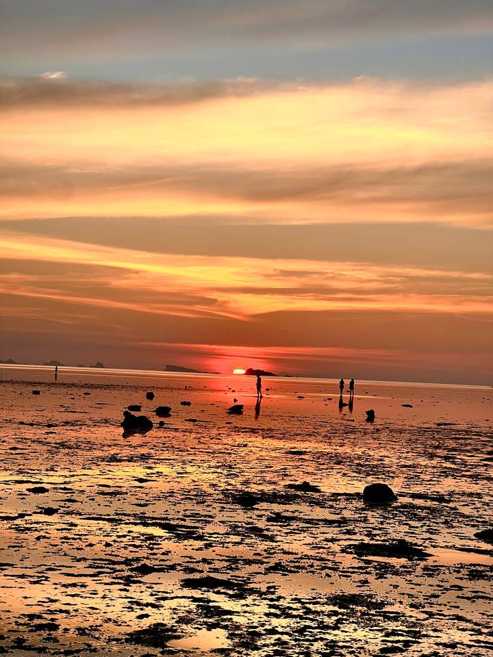 Red sun sinking below the horizon over a shallow sea with scattered rocks.