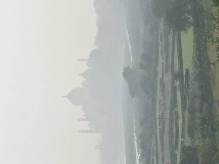 Hazy silhouette of the Taj Mahal barely visible through thick morning fog.