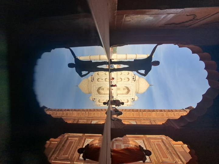 Creative reflection photo of a visitor in an archway framing the Taj Mahal.