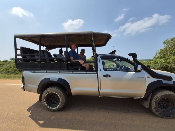 Open-sided safari jeep carrying tourists along a dusty road with green bushland behind