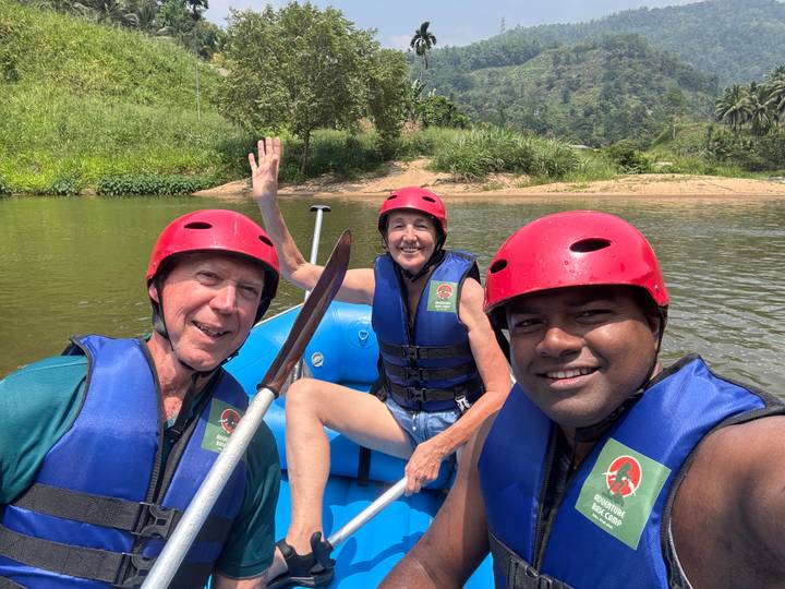 Three rafters in helmets smiling for a selfie while floating on a calm jungle river