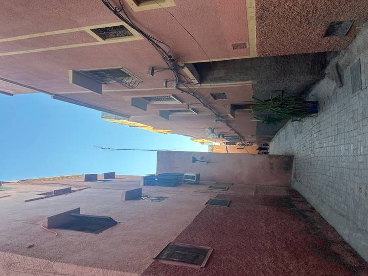 Narrow pink-washed alleyway in Marrakesh medina with cables, windows and potted plants.