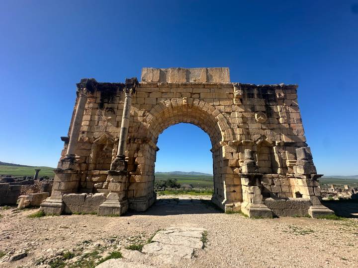 Ancient Roman triumphal arch standing intact against a bright blue sky at Volubilis.
