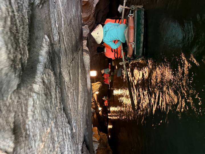 Rowboats paddle through a low cave tunnel in Trang An with reflections on the green water.