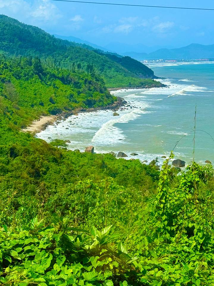 Remote coastline with waves crashing onto a green, forested headland in central Vietnam.