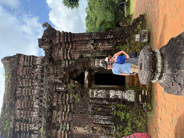 Two travellers pose before the weathered Hindu temple ruins of My Son Sanctuary.