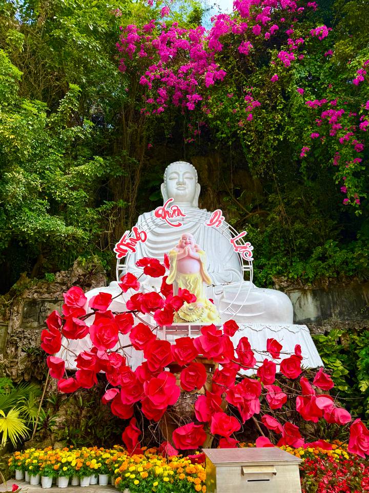 White Buddha statue with Vietnamese calligraphy backdrop surrounded by vibrant red artificial roses.