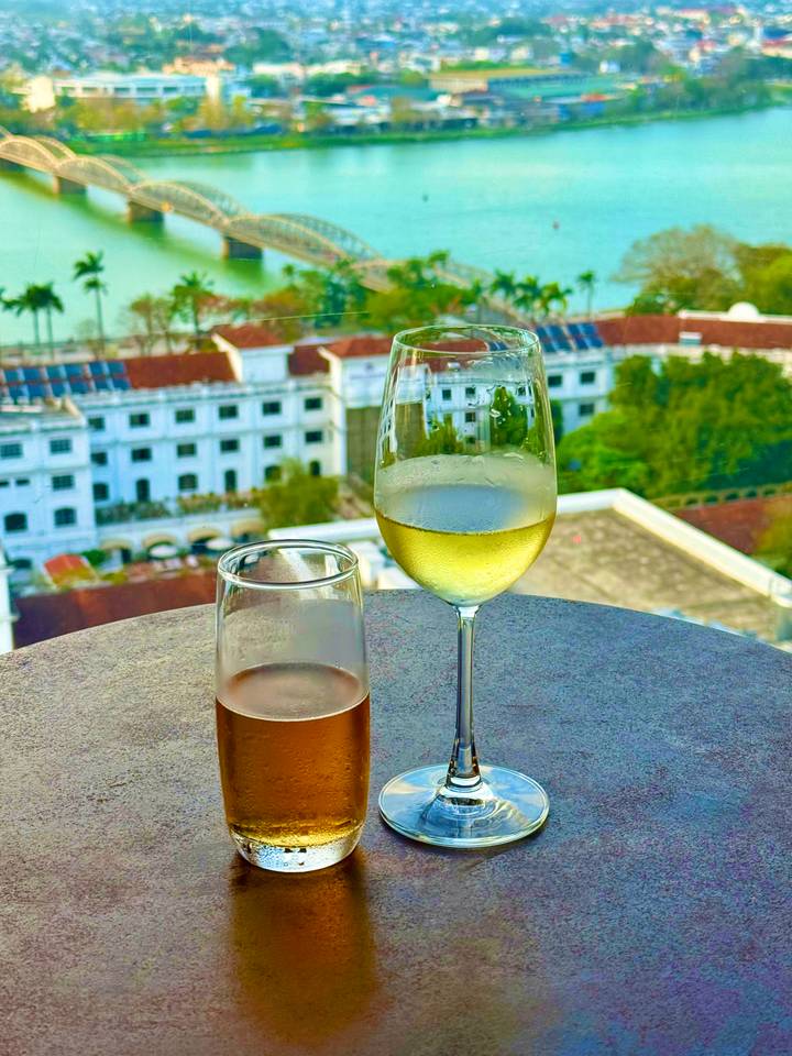 Close-up of chilled wine glasses on a rooftop bar table overlooking historic buildings in Ho Chi Minh City.