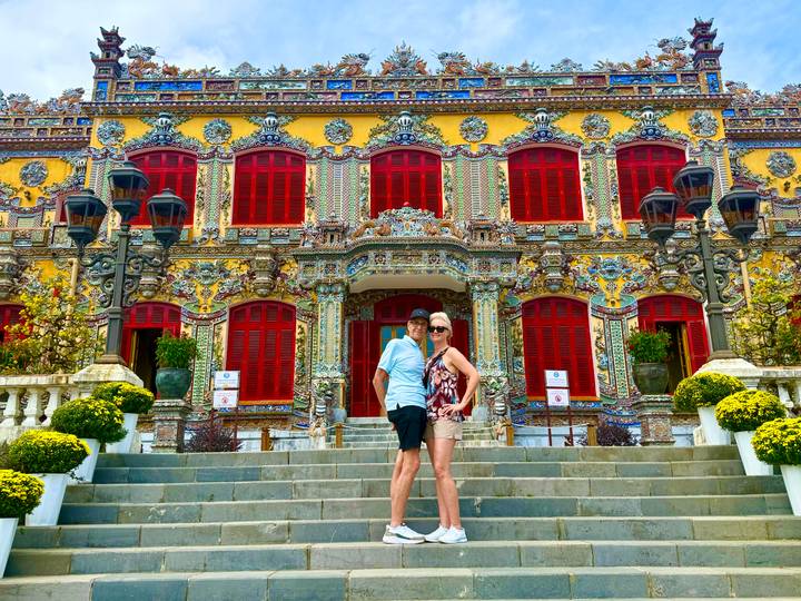Travelling couple stands on the steps of a vibrantly decorated imperial building in Hue.