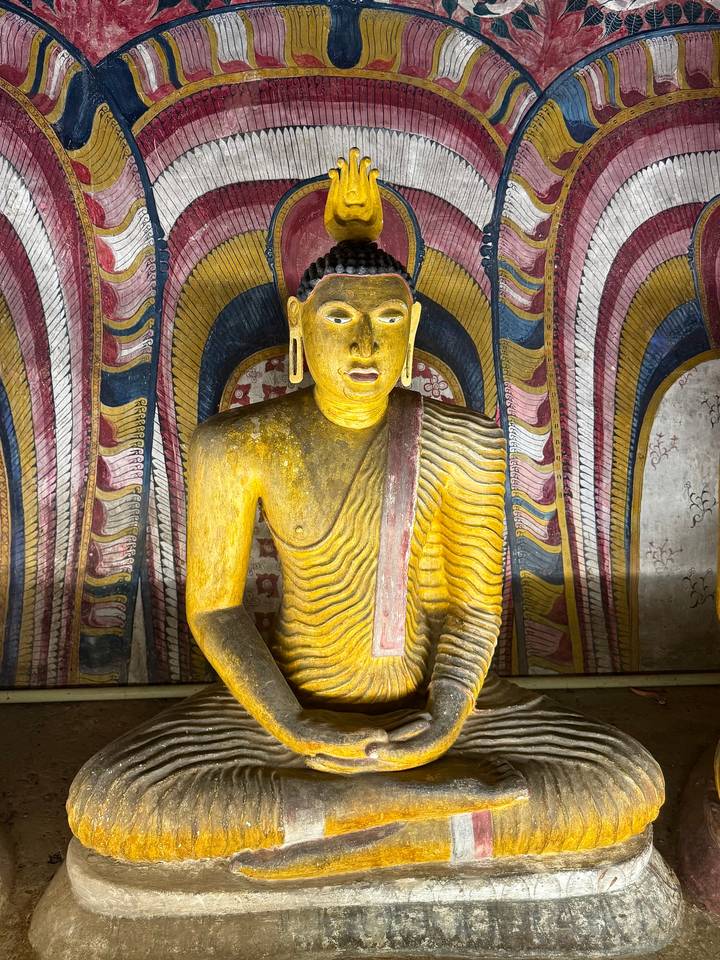 Golden Buddha statue illuminated inside a richly painted chamber at Dambulla Cave Temple.
