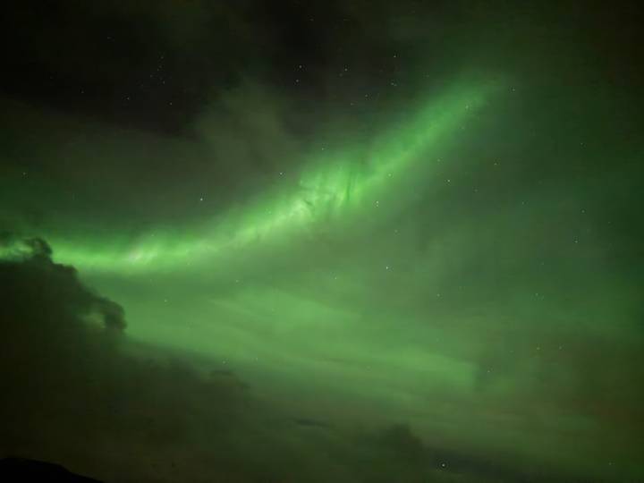 Bright green ribbon of aurora stretching across a starry Arctic sky.