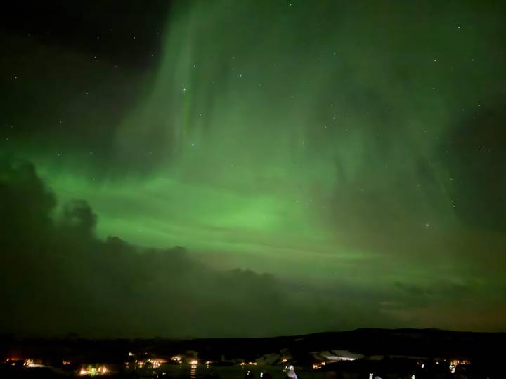 Faint curtains of green aurora glow in a cloud-streaked Arctic night sky.