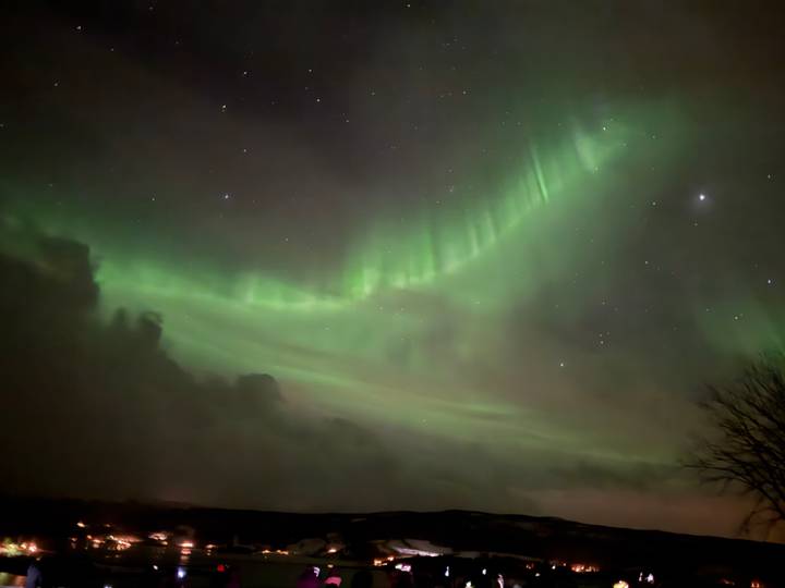 Brilliant steps of green aurora lighting up a clear starry sky above dark clouds.