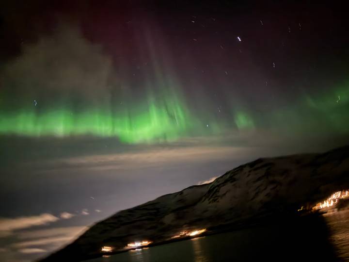 Blurry image of green aurora streaks above a snowy mountain slope at night.