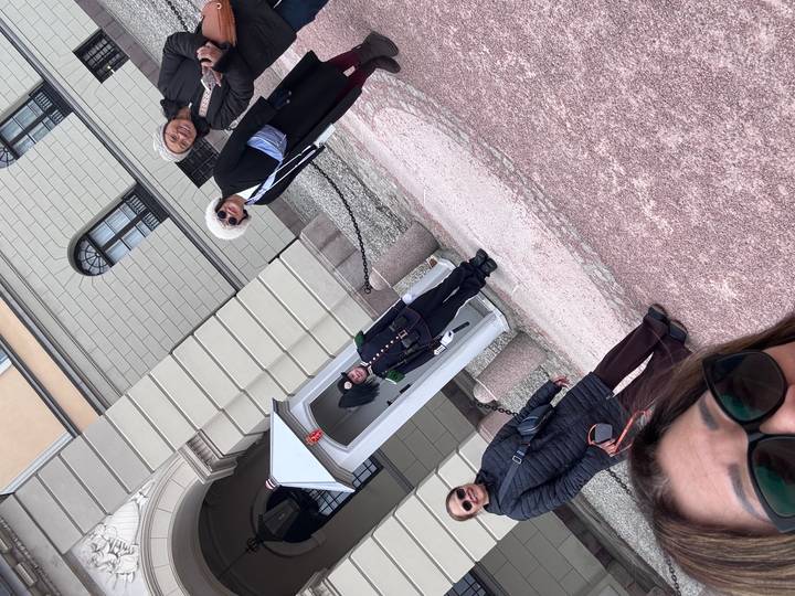 Four travellers pose beside a uniformed palace guard at a small white guardhouse outside an ornate building.