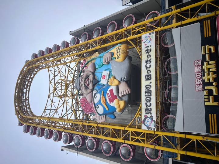 Tall yellow Ferris wheel with a cartoon mascot dominates the facade of a Don Quijote store.