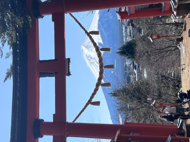 Snow-capped Mount Fuji perfectly framed by a red torii gate and sacred rope on a clear day.