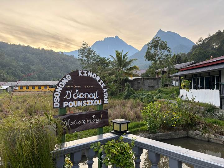 Homestay signboard in rural village with Mount Kinabalu peaks at sunrise.