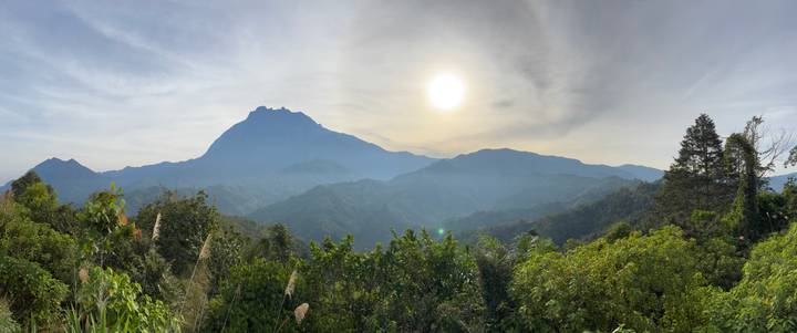 Bright sun over rolling green valleys with imposing Mount Kinabalu in haze.