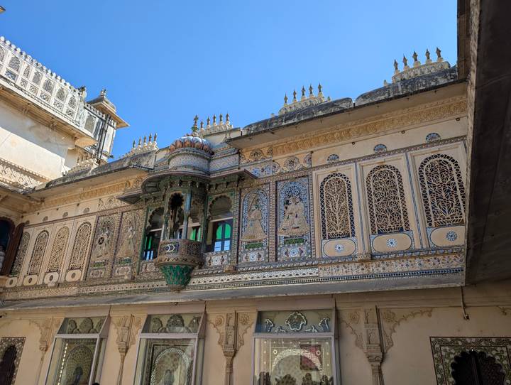 Ornately decorated facade with mosaics and jharokha balcony inside Udaipur City Palace.