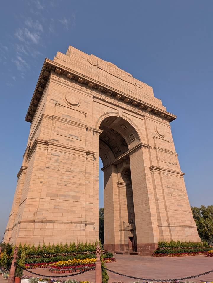 Sandstone India Gate war memorial in New Delhi rises against a cloudless blue sky.