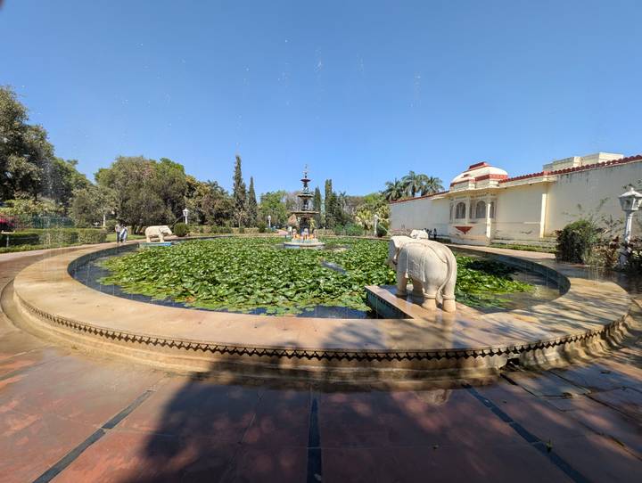 Circular lily pond with playful stone elephant fountains in a landscaped heritage garden.