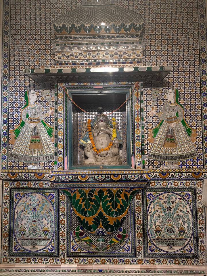 Ornate Ganesh shrine framed by colorful Rajasthani tile mosaics inside a palace museum.