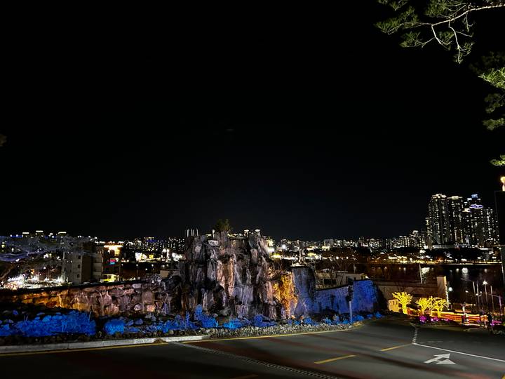 Night city skyline behind illuminated rocky sculpture with lights twinkling across horizon.