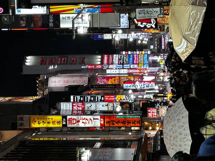 Crowded Tokyo street at night filled with umbrellas and towering neon signboards.