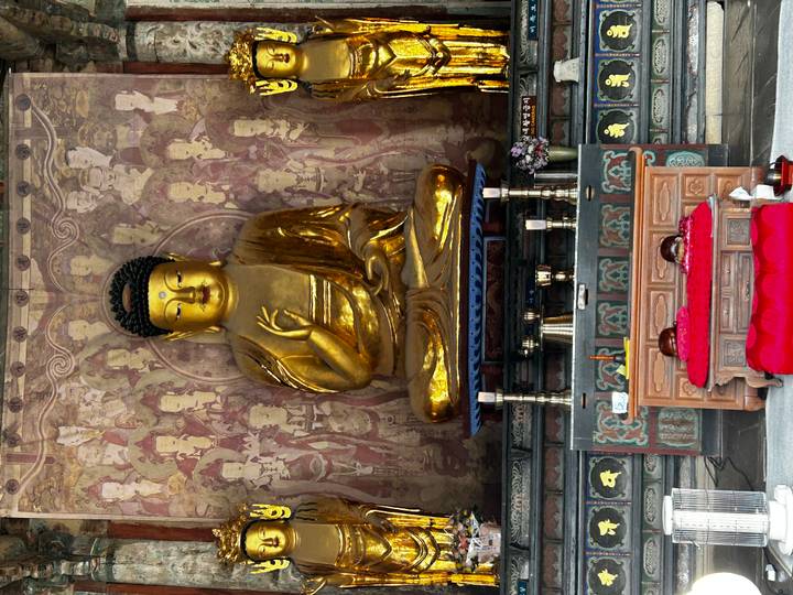 Large golden seated Buddha statue inside richly decorated temple shrine.