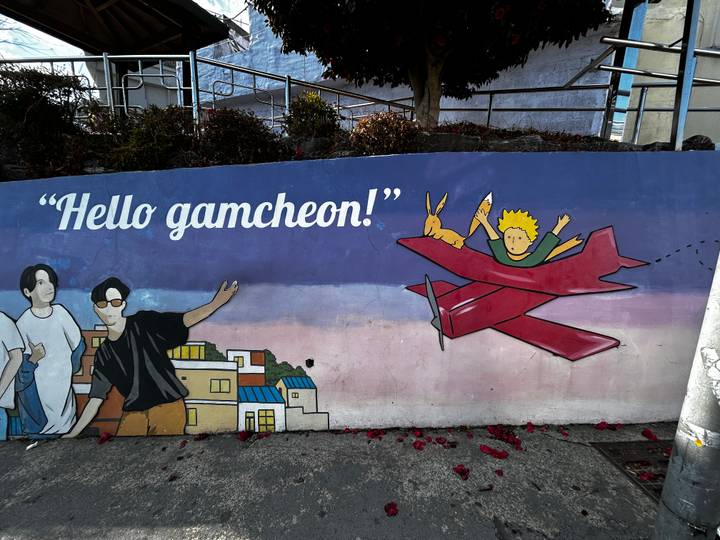 Colourful street mural reading 'Hello gamcheon!' with cartoon characters and red plane.