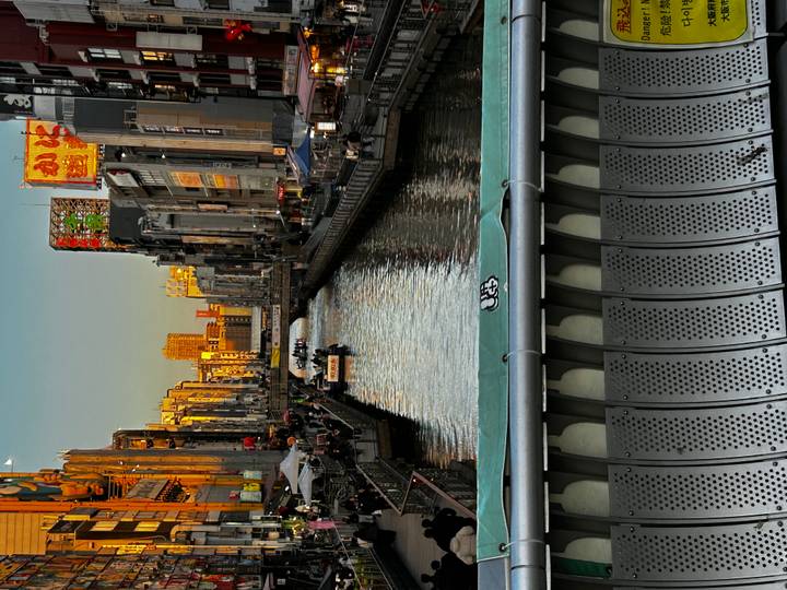Evening light reflects on canal lined with neon-lit buildings and bridges in Osaka.