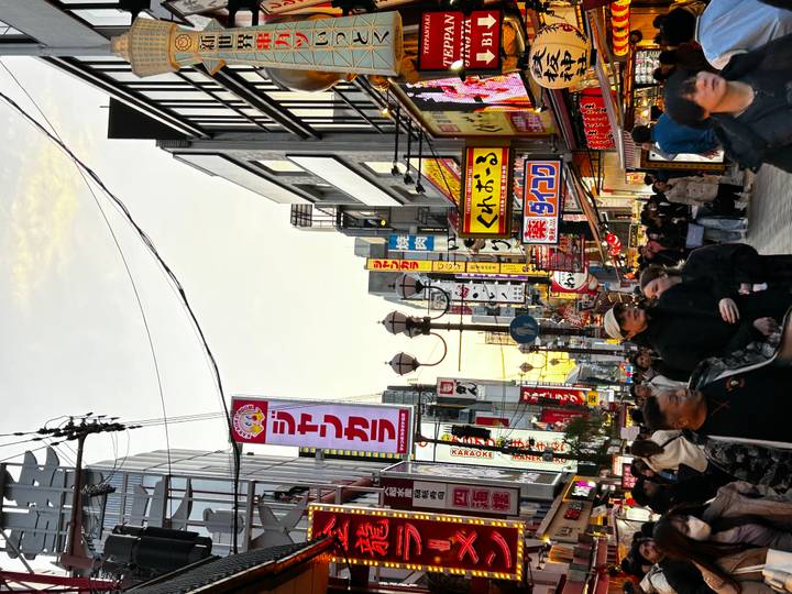 Crowded shopping street lined with colourful signs and busy pedestrians at dusk.