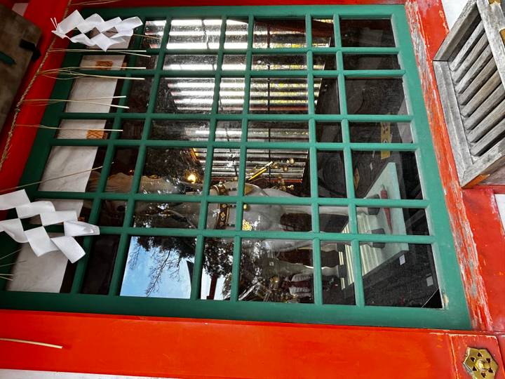 White horse statue displayed behind green lattice window of Shinto shrine building.