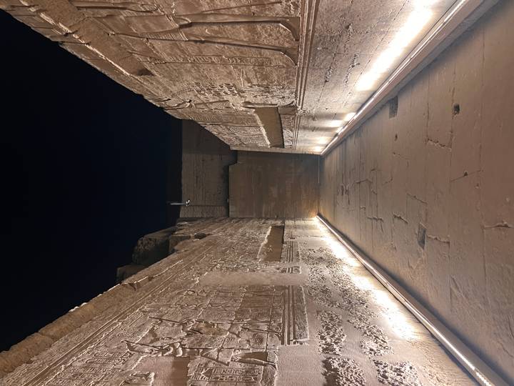 Narrow temple corridor illuminated from below, revealing detailed hieroglyphic reliefs on both walls.