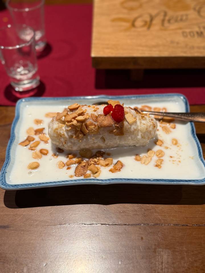 Vietnamese dessert of banana in sweet coconut milk garnished with peanuts and a red cherry.