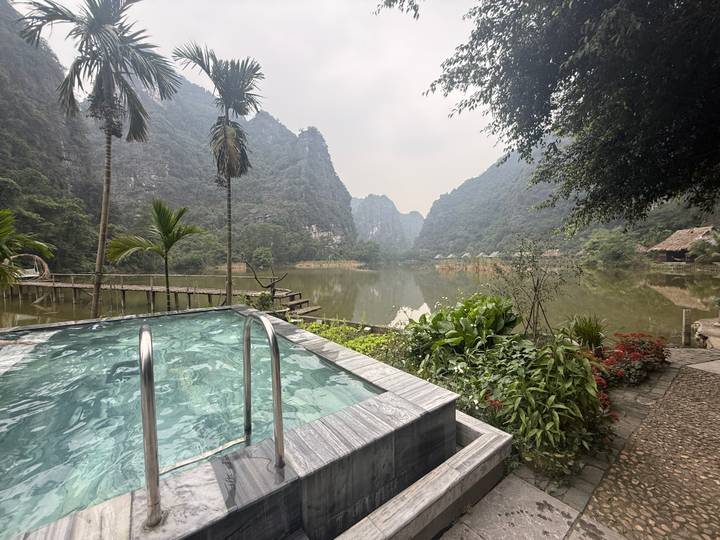 Infinity pool overlooking a tranquil lake surrounded by limestone cliffs and lush vegetation in Ninh Binh.