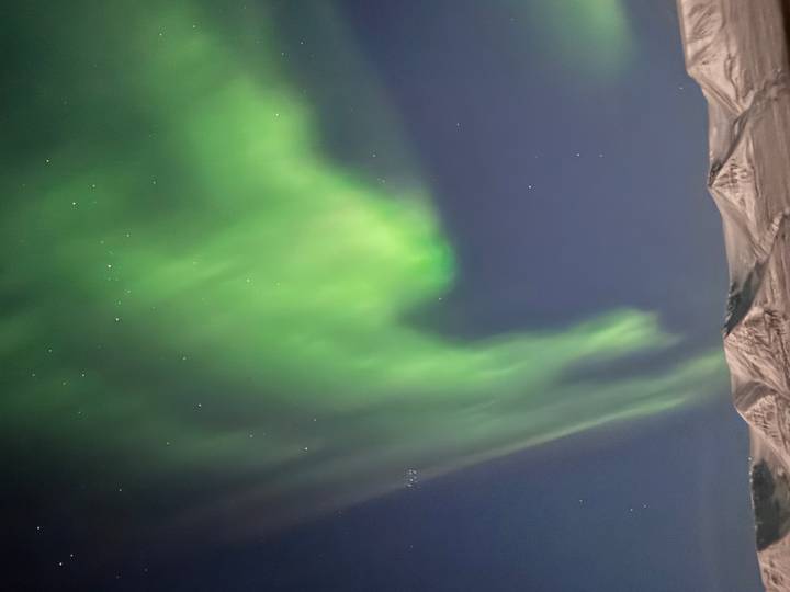 Vivid green northern lights swirl above snow-covered mountain ridges beneath a clear night sky.
