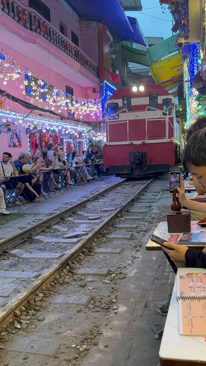 Tourists sit at tiny tables along Hanoi’s Train Street as a red train carriage inches past.