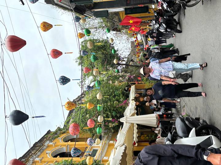 Lantern-festooned street in Hoi An Old Town with locals and tourists walking beneath colourful lamps.