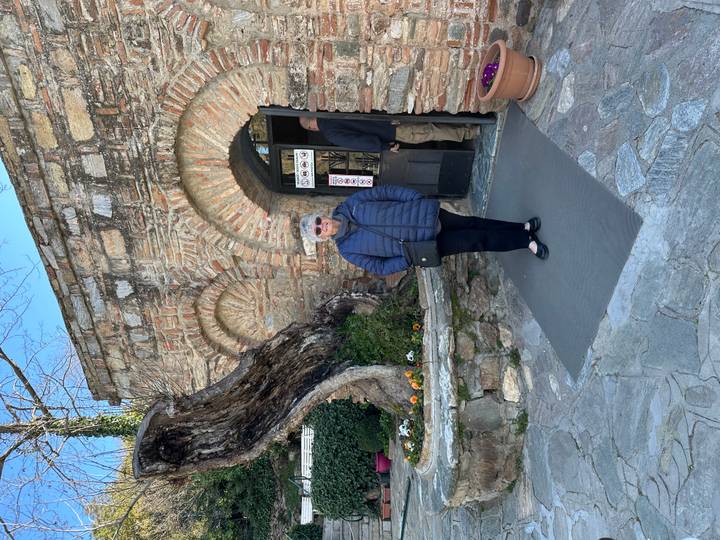 Woman stands outside a historic stone building with arched doorway and flowers.